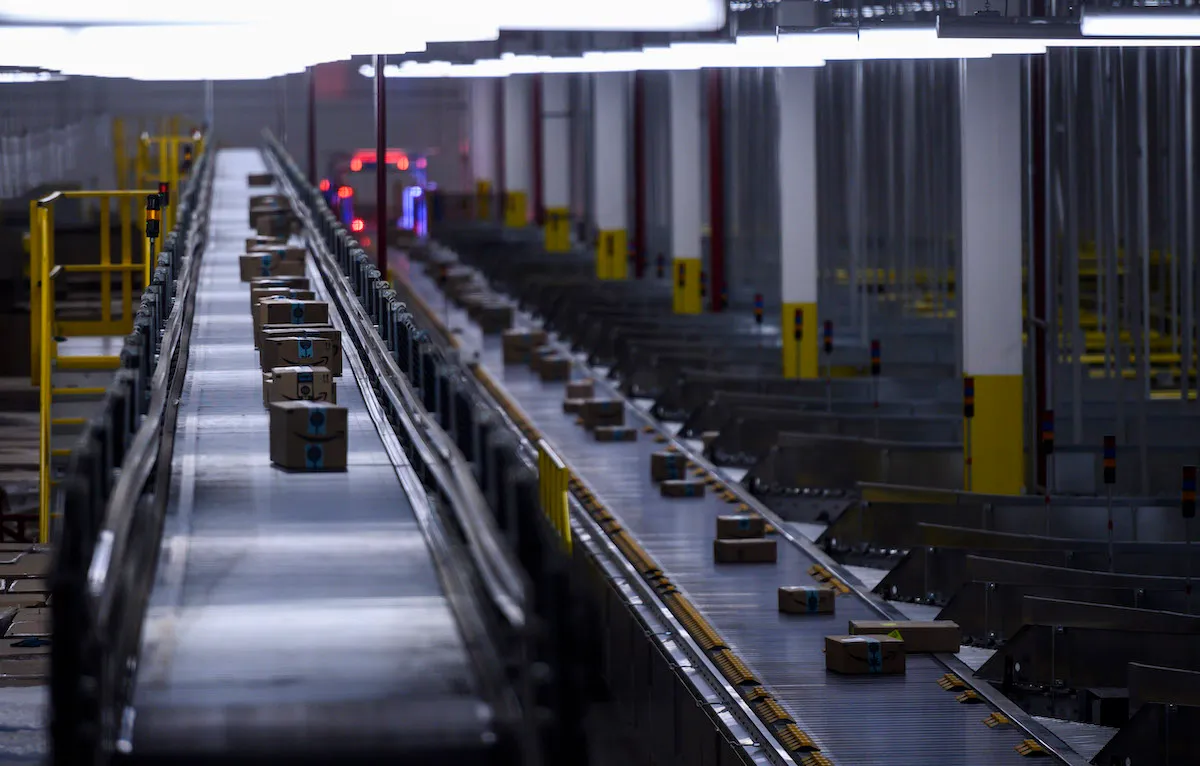 Amazon packages on a conveyor belt in a factory room.