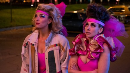 Debbie (Betty Gilpin) and Ruth (Alison Brie) stand on the street in bright pink 80s wrestling costumes.