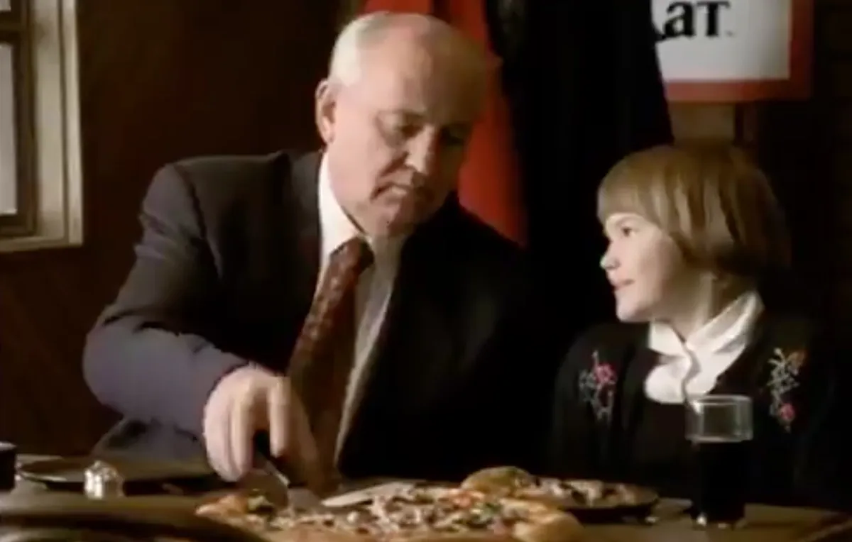 Gorbachev inexplicably eats Pizza Hut pizza with a happy child.