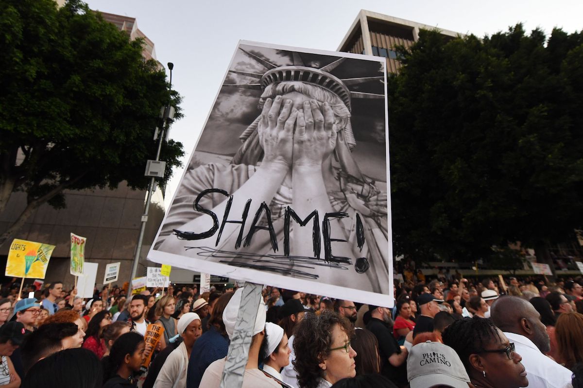 A protestor holds a picture of the Statue of Liberty crying, with the word SHAME written across it.