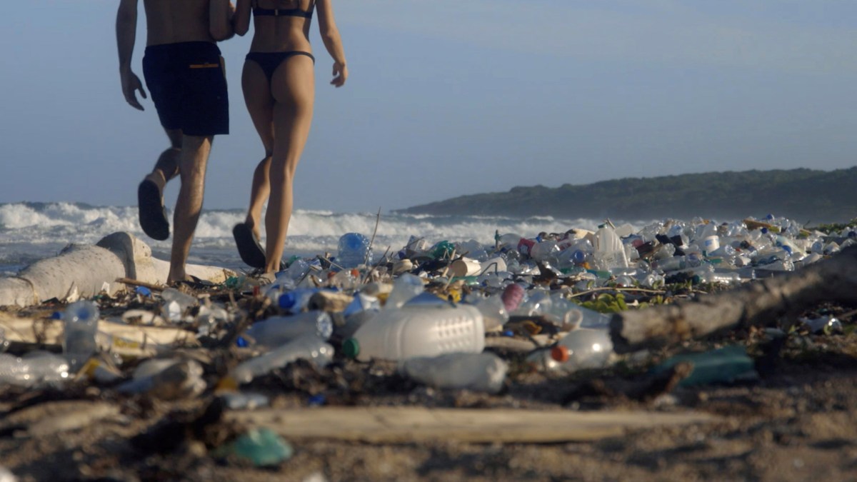A man and woman walk on a beach covered in trash.