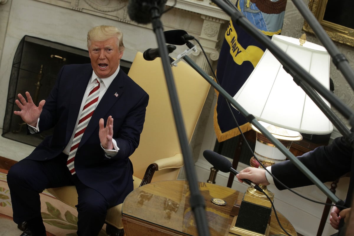 Donald Trump rants in the Oval Office, surrounded by reporters' microphones.