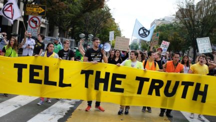 Climate protesters carry a large banner reading 'TELL THE TRUTH.'
