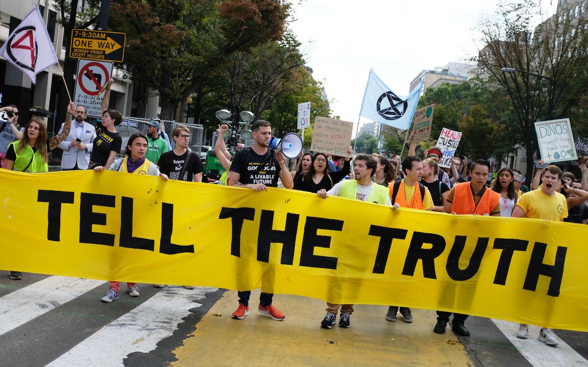 Climate protesters carry a large banner reading 'TELL THE TRUTH.'