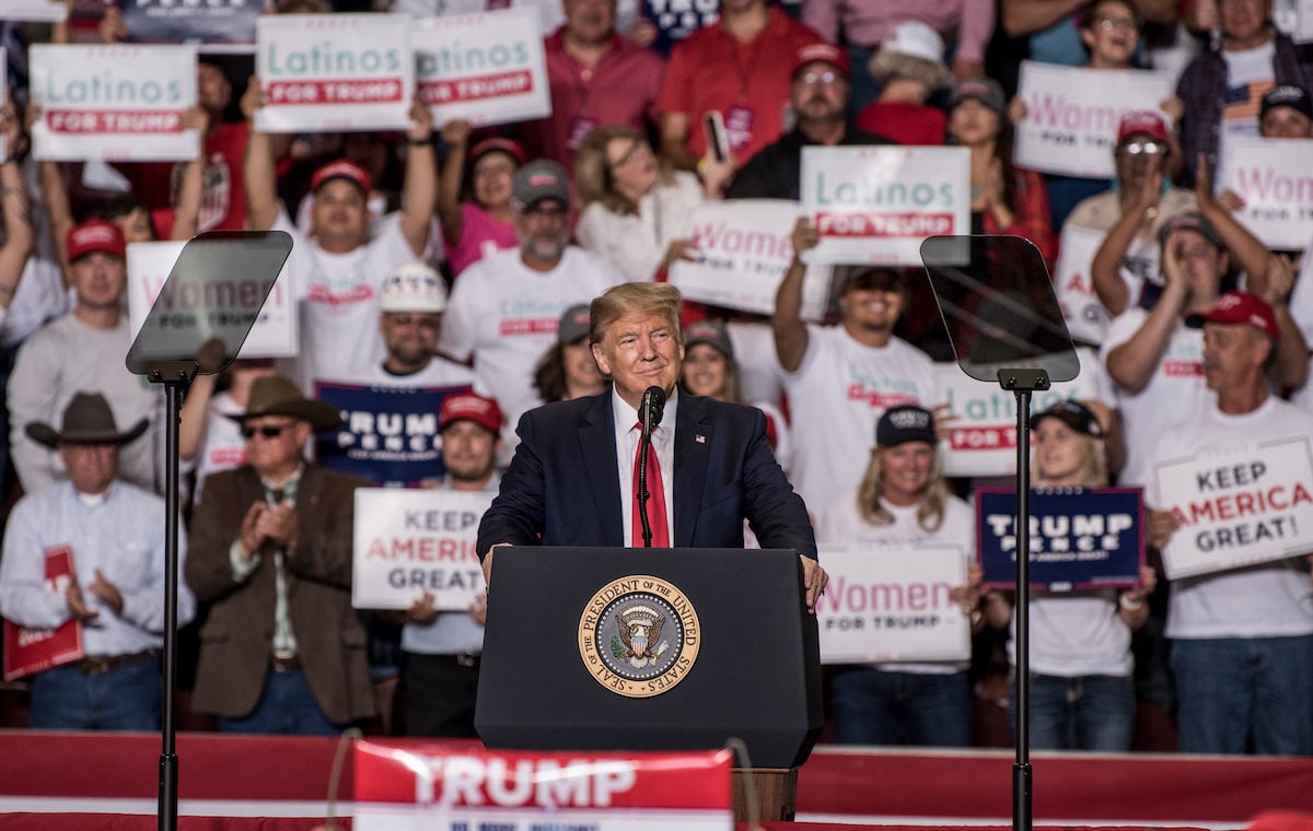 Donald J. Trump speaks at a rally with supporters holding Latinos for Trump signs behind him.