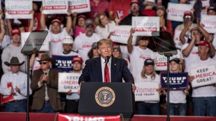 Donald J. Trump speaks at a rally with supporters holding Latinos for Trump signs behind him.