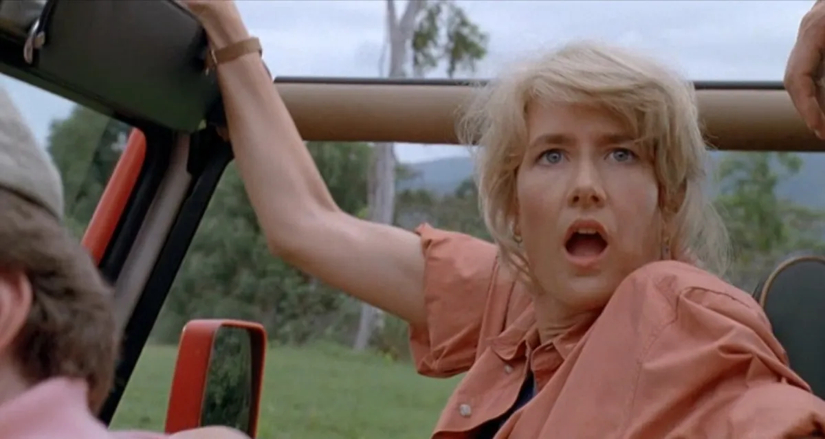 A white woman rises up out of her seat in a jeep with a surprised look on her face in "Jurassic Park"