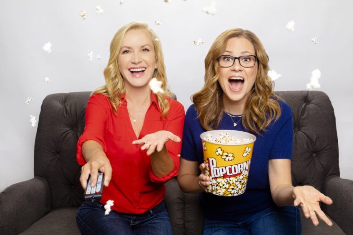 Angela Kinsey and Jenna Fischer sit together on a couch, holding popcorn.