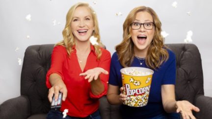 Angela Kinsey and Jenna Fischer sit together on a couch, holding popcorn.