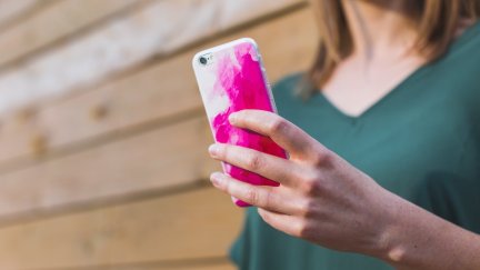 A woman's hand holds a smartphone in a pink case.