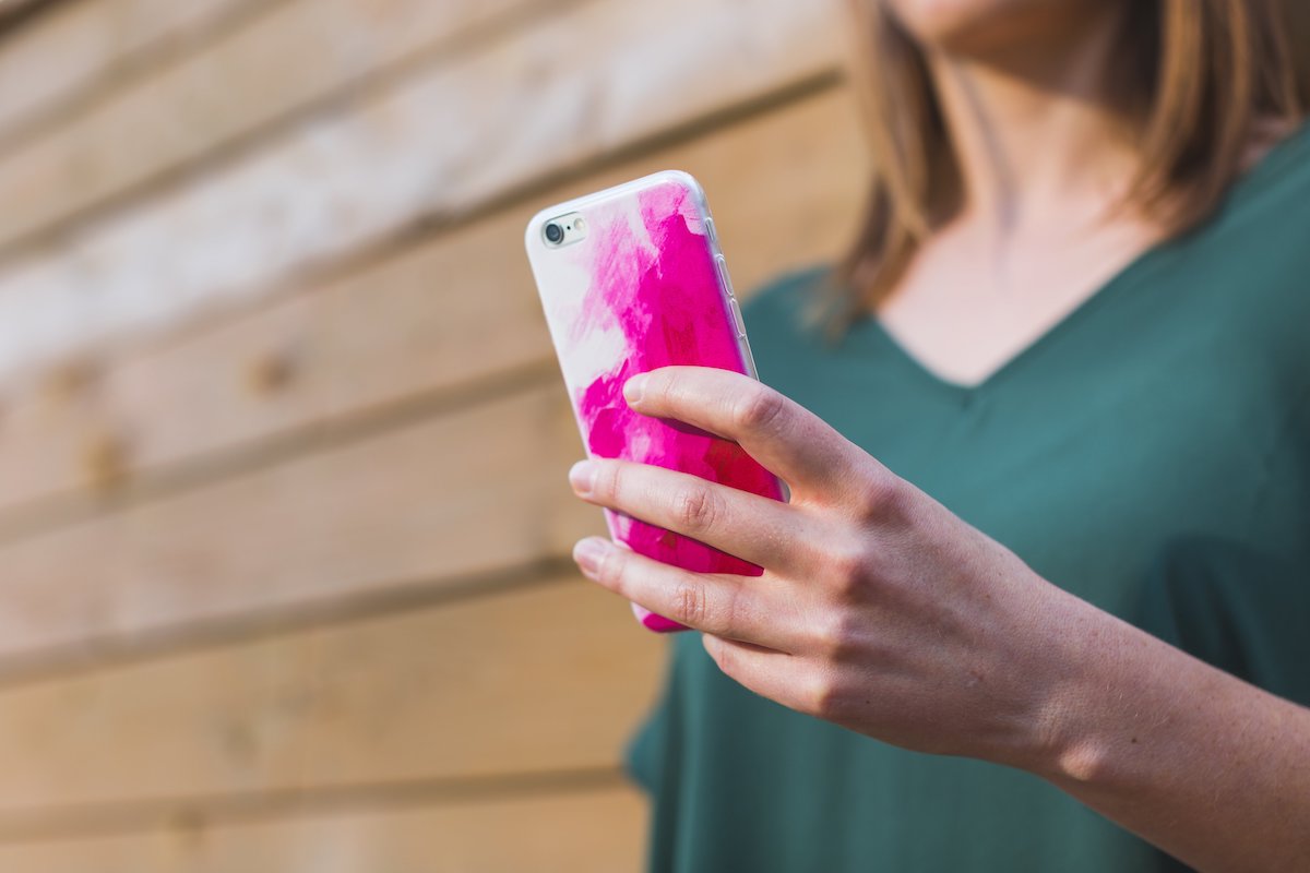 A woman's hand holds a smartphone in a pink case.