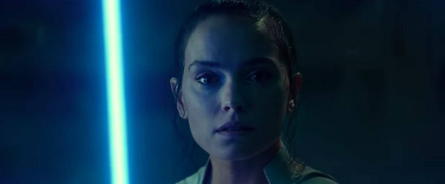 Rey stares into the camera, holding up a blue lightsaber in Star Wars: The Rise of Skywalker trailer.