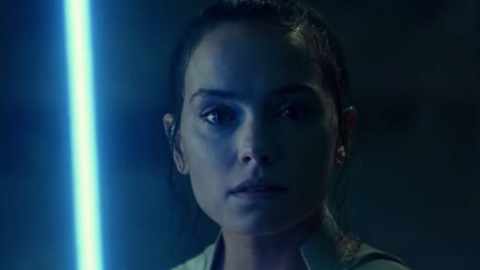 Rey stares into the camera, holding up a blue lightsaber in Star Wars: The Rise of Skywalker trailer.