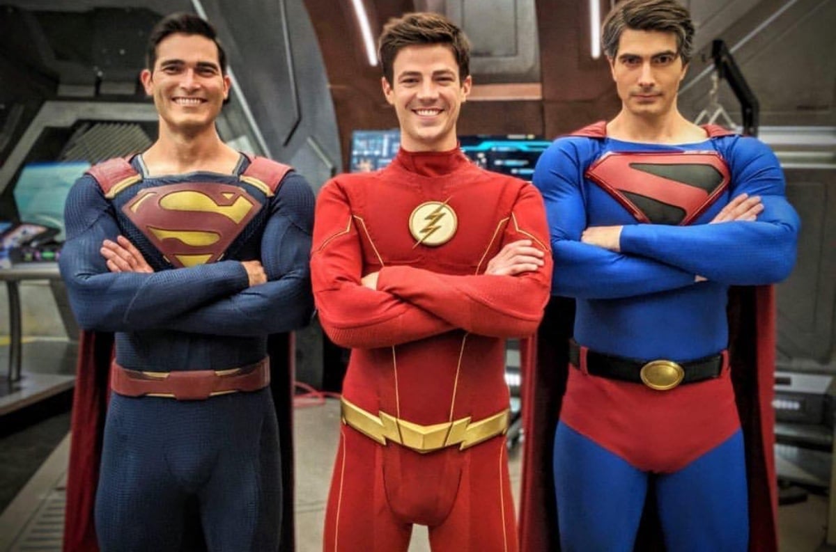 Grant Gustin's The Flash centered between Tyler Hoechlin and Brandon Routh, with both actors dressed in their Superman costumes.