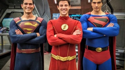 Grant Gustin's The Flash centered between Tyler Hoechlin and Brandon Routh, with both actors dressed in their Superman costumes.