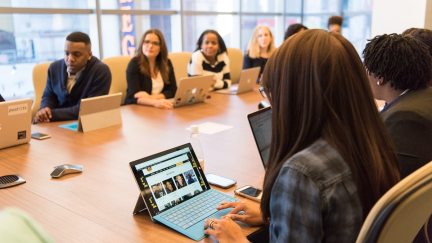 Young people sit around a conference table looking at laptops.