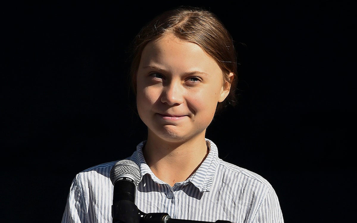 Greta Thunberg smiles at a microphone.