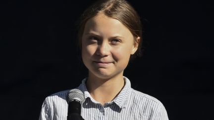 Greta Thunberg smiles at a microphone.