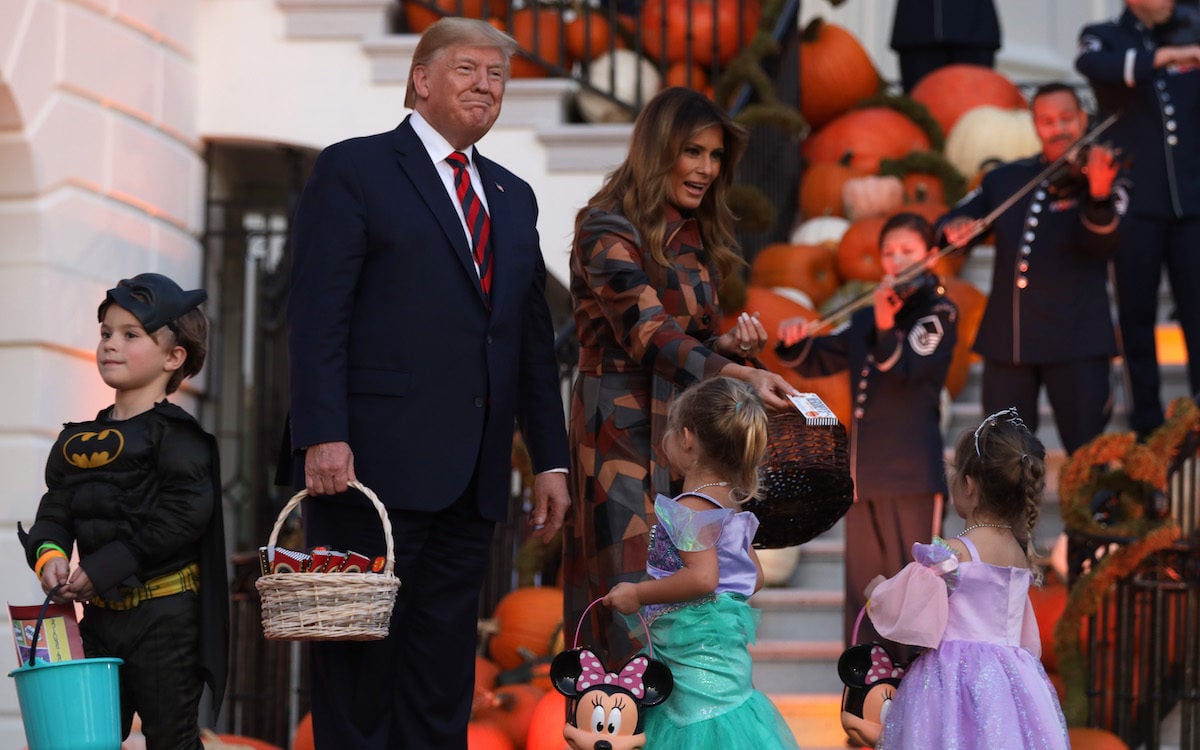 Donald Trump smiles awkwardly around children in Halloween costumes outside the White House.