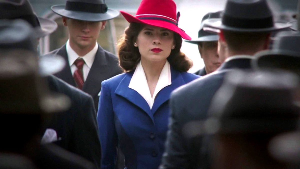 Peggy Carter in her colorful outfit, walking in a crowd of grey suits in Marvel's Agent Carter.