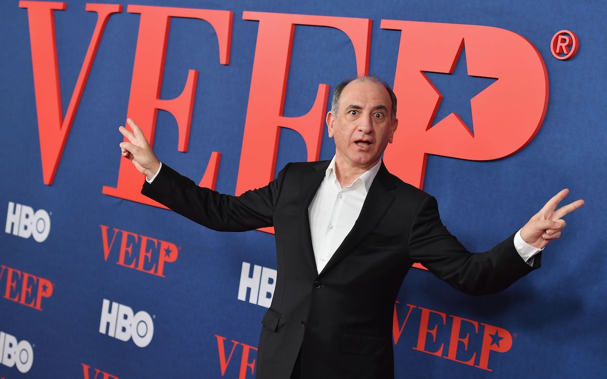 Armando Iannucci does the Nixon peace sign pose in front of the VEEP logo.