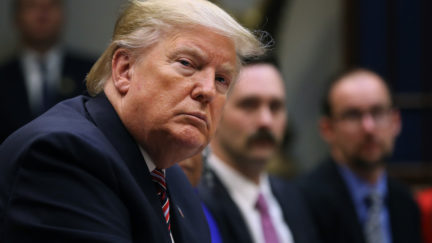 Donald Trump sits at a roundtable, looking at the camera suspiciously.