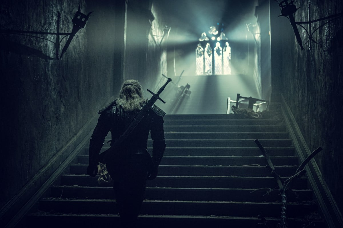 Henry cavil and gerralt walks up spooky stairs in The Witcher.