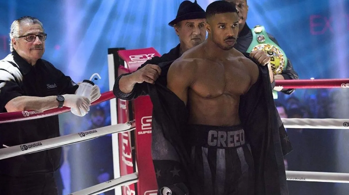 Michael B. Jordan taking his robe off in a boxing ring in Creed II.