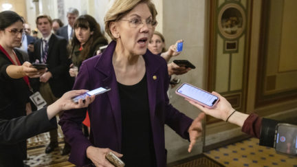 Elizabeth Warren talks to reporters in the hallway of the impeachment trial.