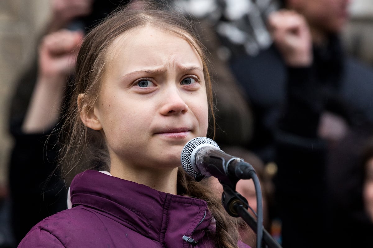 Greta Thunberg stands at a microphone and frowns.