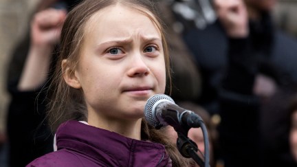 Greta Thunberg stands at a microphone and frowns.