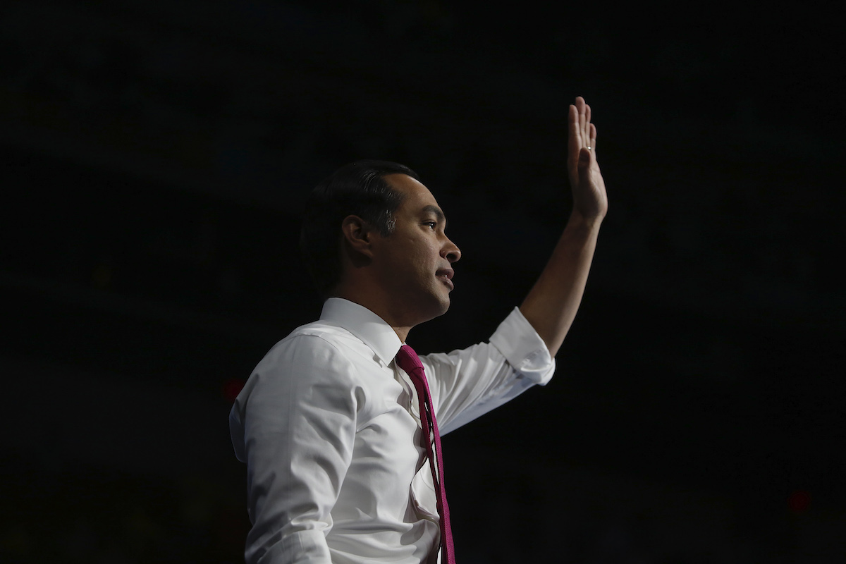 Julian Castro waves in profile in front of a black background.