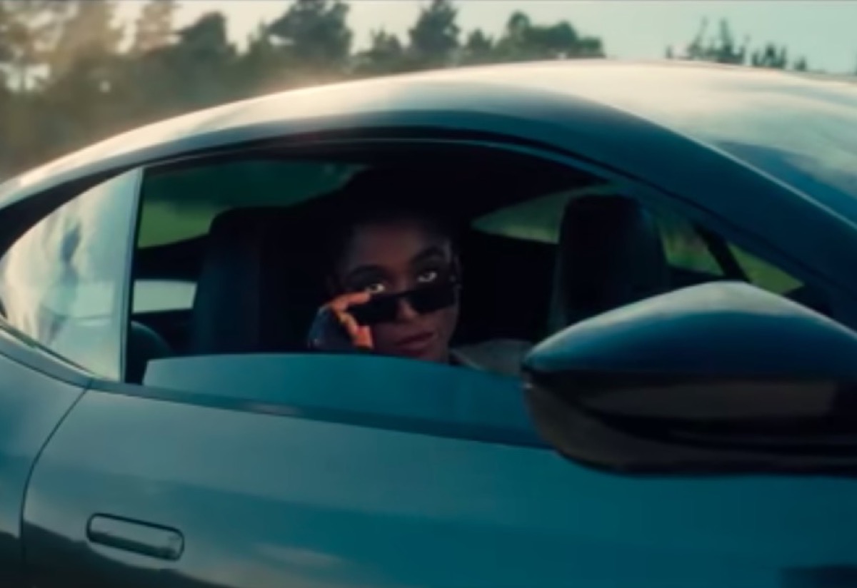 Lashana Lynch looks pointedly over the top of her sunglasses at Bond, peering out the window of a fancy car.