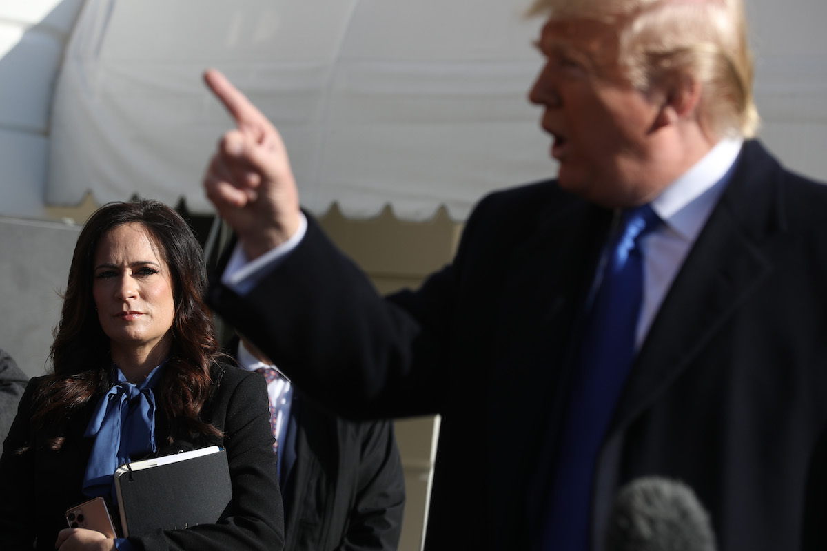 White House Press Secretary Stephanie Grisham (L) listens to U.S. President Donald Trump talk to reporters