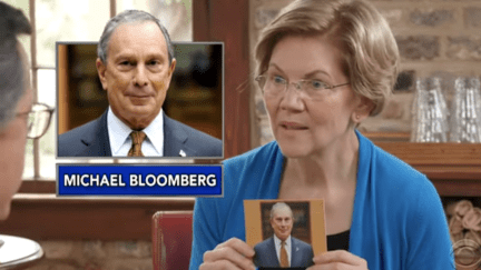 Elizabeth Warren holds up a picture of Mike Bloomberg during 