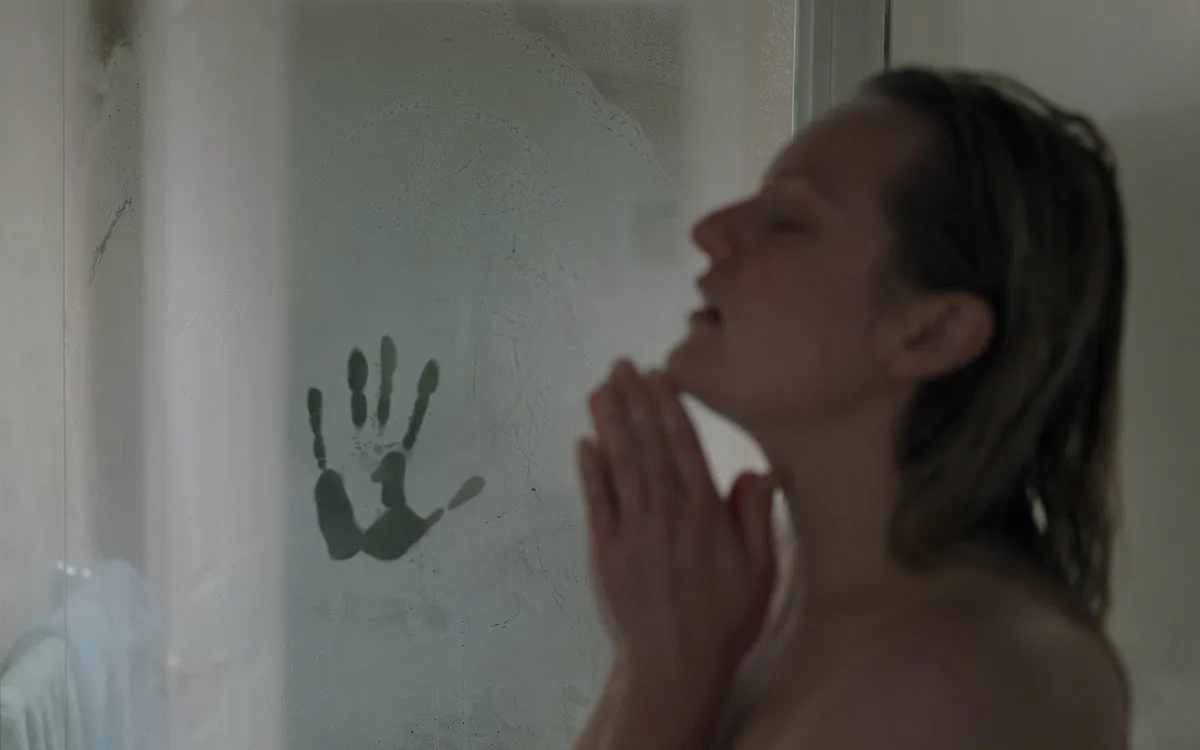 Elizabeth Moss takes a shower with a handprint in the steam.
