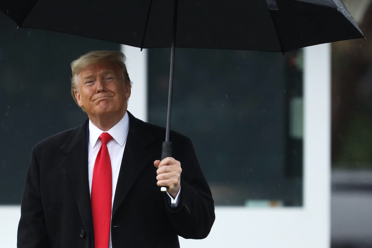 Donald Trump smiles as he holds an umbrella.