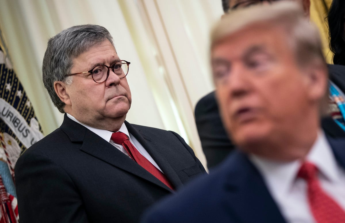 Attorney General William Barr frowns at Donald Trump, sitting in front of him, out of focus.