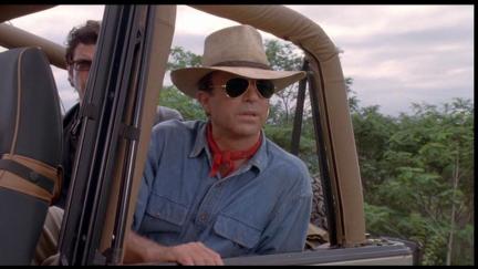A white man wearing a wide fedora and sunglasses sitting in a jeep looking into the distance in 