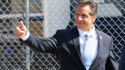 New York Gov. Andrew Cuomo gives a thumbs-up in front of a chainlink fence.