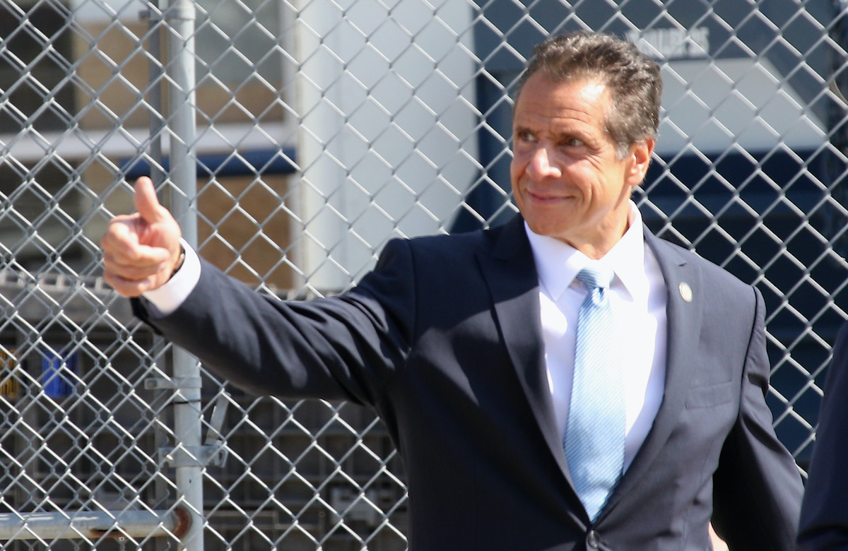 New York Gov. Andrew Cuomo gives a thumbs-up in front of a chainlink fence.