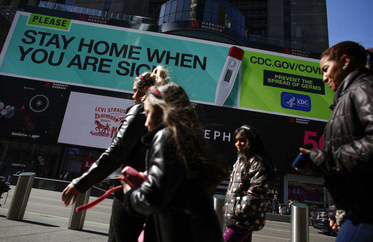 People walk past a sign that advises people to stay home in Times Square
