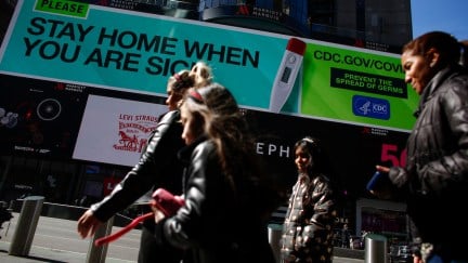 People walk past a sign that advises people to stay home in Times Square