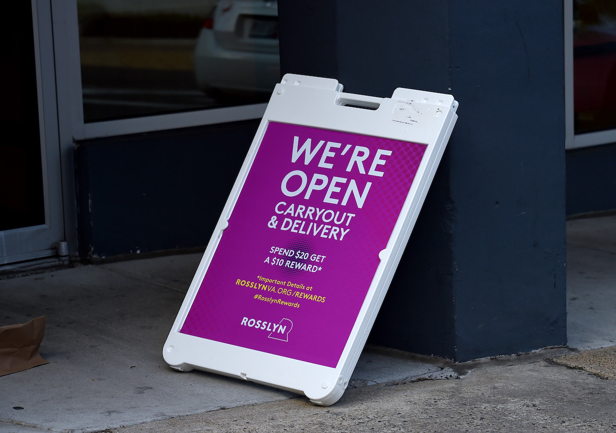 Carry out/delivery only sign leans against the wall outside of a restaurant.