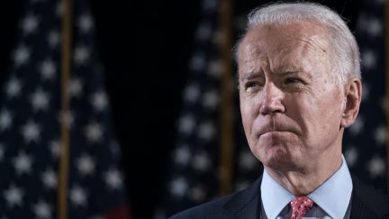 Joe Biden stands in front of a row of flags.