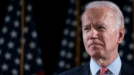 Joe Biden stands in front of a row of flags.