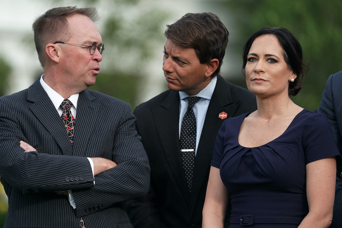 Stephanie Grisham stares at the camera while two men talk