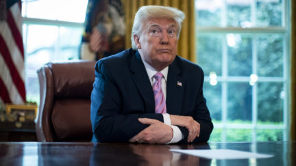 Donald Trump folds his arms and sits at the Oval Office desk.