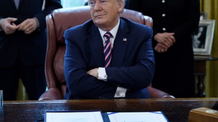 Donald Trump folds his arms and looks smug sitting behind the Oval Office desk.