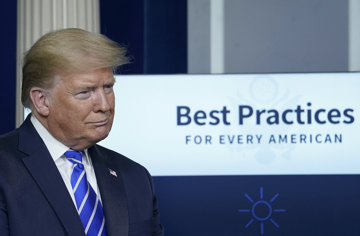 Donald Trump stands in front of a sign reading 'Best Practices for every American' during press briefing.